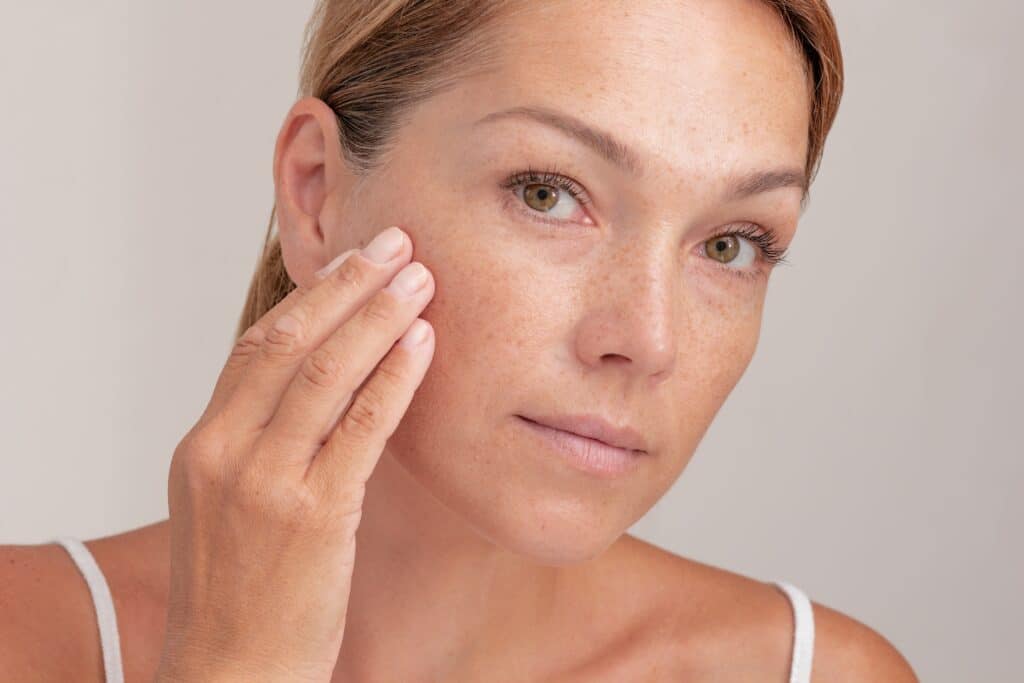 Portrait of cropped caucasian middle aged woman face with freckles touching skin by hand
